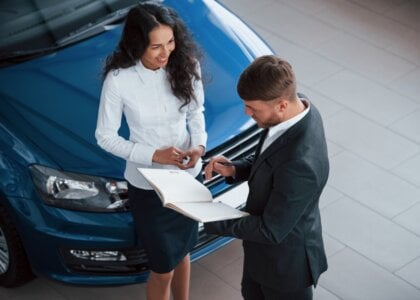 Vendedor y clienta revisando documentos frente a coche azul
