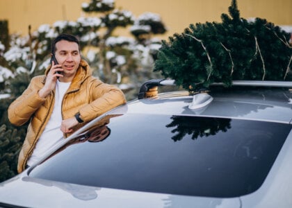 Handsome man talking on phone by the car with christmas tree on top