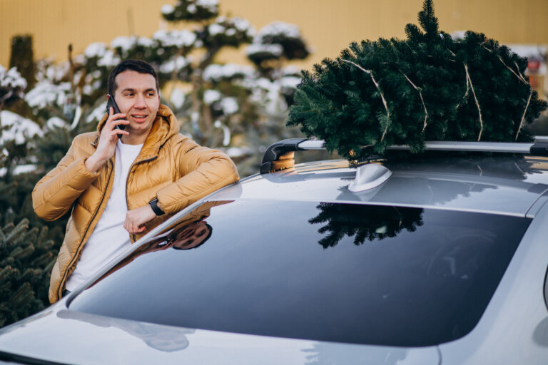 Handsome man talking on phone by the car with christmas tree on top